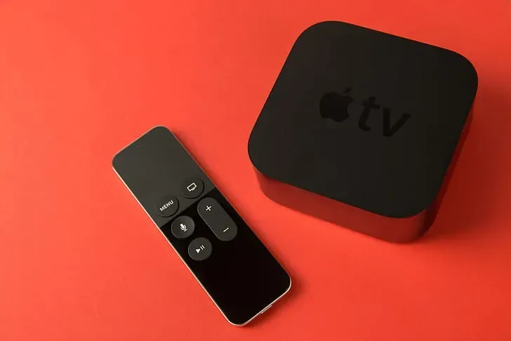 An Apple TV box and its remote on a red table